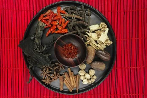 Mix composition of various exotic dried spices in black round bowl on red bam Stock Photos