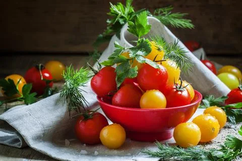 Mix red and yellow cherry tomatoes, parsley and dill in red bowl, dark wood b Foto stock