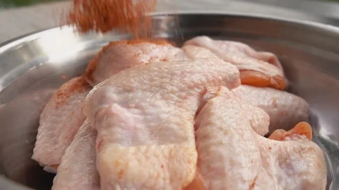 Mix of spices is falling on the chicken wings in the metal bowl Stock Footage 148348812
