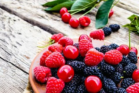 Mixed berries of raspberry, cherry, mulberry in a bowl on wooden background. Stock Photos