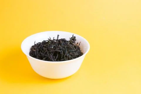 Mixed black tea in little white bowl on a yellow background, copy space Stock Photos