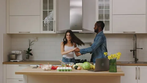 Mixed couple in the kitchen at home. The man and woman dance and fool around Stock Footage 236253632