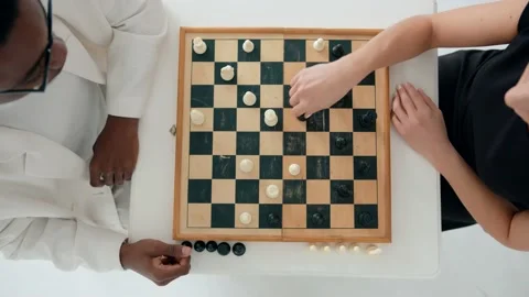 A mixed couple is playing chess and a caucasian girl knocks down an opponent's 库存影片 174834372