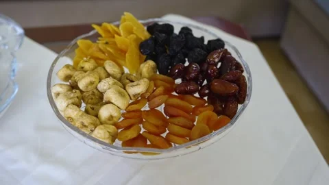 Mixed dried fruit and nuts in a glass bowl on a white tablecloth in a living Stock Footage 334979825