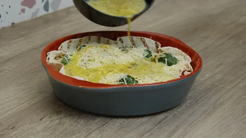 Mixed eggs are being poured on cheese, tomatoes and spinach in a baking dish. Stock Footage 266423038
