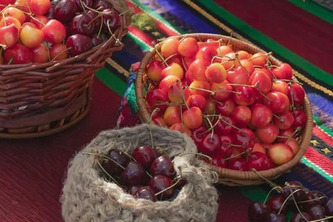 Mixed fresh cherries in rustic baskets and woven bag on traditional textile.. Stock Photos