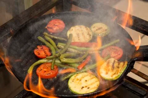 Mixed grilled vegetables on a pan. Fire and smoke present during cooking.  Stock Photos
