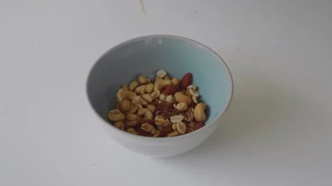 Mixed nuts falling into a bowl on a white background Video stock 320790103