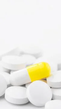 Mixed pile of yellow round tablets and white oval medicinal capsules scattere Stock Photos