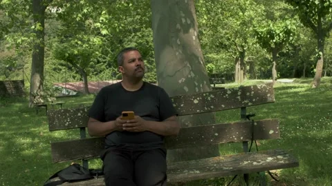 A mixed race black middle-aged adult man sits on a bench in the park or forest Stock Footage 157533965