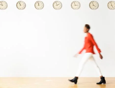 Mixed race businesswoman walking under clocks Stock Photos