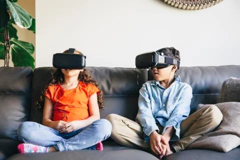 Mixed race children using virtual reality goggles on sofa Stock Photos