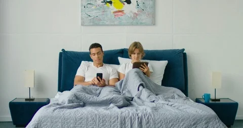 Mixed race couple is lying in bed, browsing in gadgets Stock Footage 114918022
