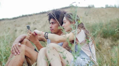 Mixed race couple sitting on the grass and selects pictures in your smartphone Stock Footage 57106281