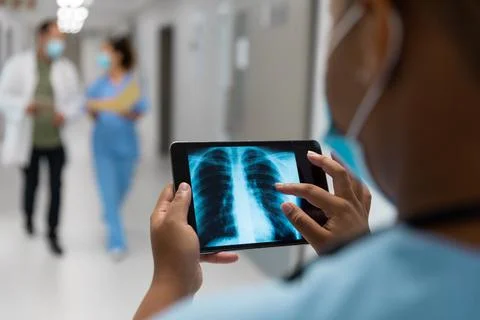 Mixed race doctor in corridor wearing face mask looking at lung x-ray on tablet Stock Photos