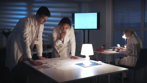 Mixed race electronics engineers in white coats discussing control electronics 库存照片