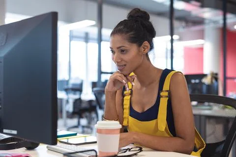 Mixed race female creative worker sitting at desk using computer Stock Photos