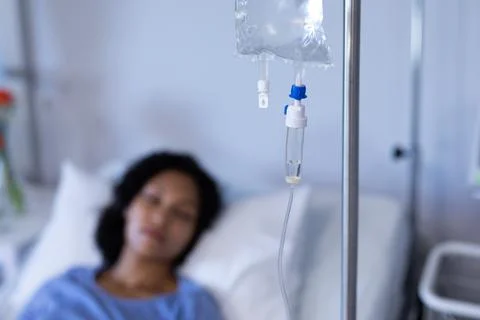 Mixed race female patient lying asleep in hospital bed hooked up to iv drip, Stock Photos