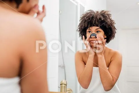 Mixed race girl applying charcoal nose patch in bathroom Stock Photos