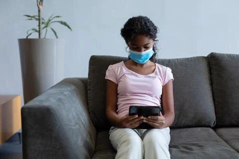 Mixed race girl wearing face mask using tablet in hospital waiting room Stock Photos