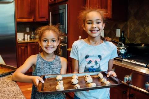 Mixed Race girls holding tray with cookie dough in domestic kitchen Stock Photos