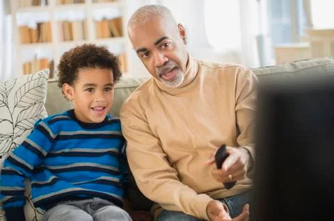 Mixed race grandfather and grandson watching television Stock Photos