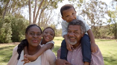 Mixed race grandparents piggyback with grandchildren in park Stock Footage