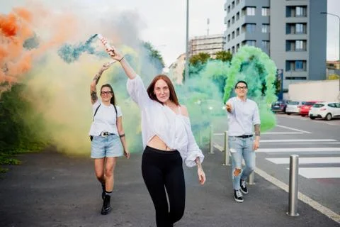 Mixed race group of friends hanging out together in town, using colourful smoke Stock Photos