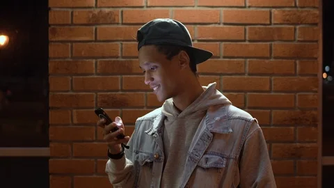 Mixed race guy chatting on his smartphone and smilling at night time in the city Stock Footage 115824288