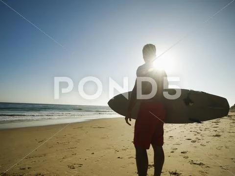 Mixed Race Man Carrying Surfboard On Beach