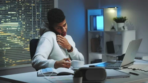 Mixed-race man working on computer, speaking by smartphone and drinking a cup of Stock Footage 143452620