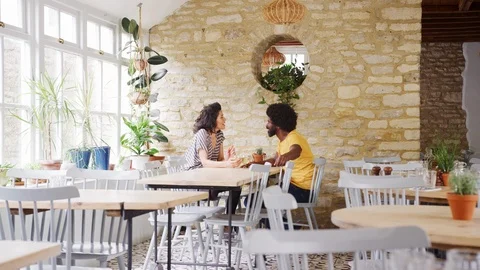 Mixed race middle aged couple sitting at table talking in an empty restaurant 스톡 동영상 99752841