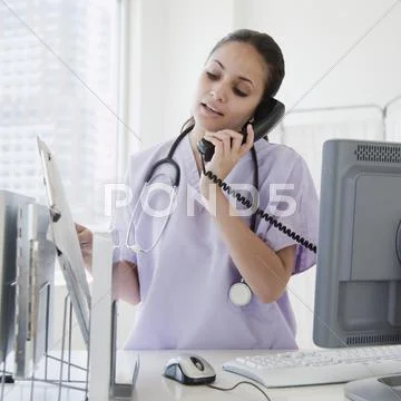 Mixed race nurse talking on telephone in hospital Stock Photos
