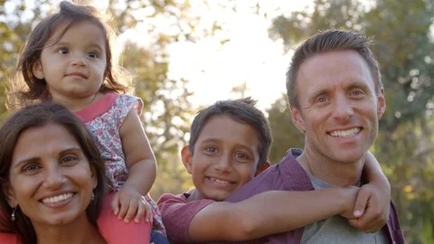 Mixed race parents carrying their kids piggyback in a park Stock Footage