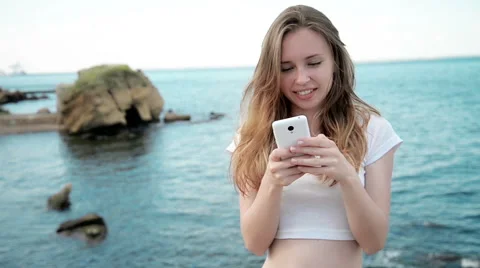 Mixed race pretty smiling young woman holding and looking at smart phone on Stock Footage 64054306