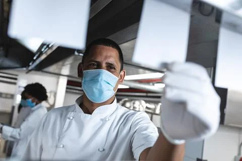 Mixed race professional chef looking at orders wearing sanitary gloves and face Stock Photos