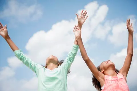 Mixed race sisters cheering in blue sky Stock Photos