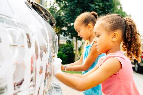 Mixed race sisters washing car Stock Photos