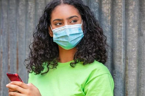 Mixed Race Teenager Girl Woman Wearing Face Mask Using Cell Phone Stock Photos