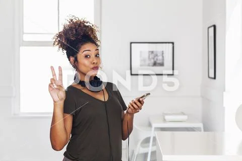 Mixed race woman holding cell phone gesturing peace Stock Photos