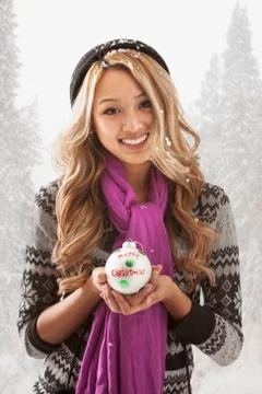 Mixed race woman holding Christmas ornament in snow Stock Photos