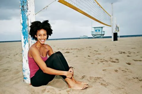 Mixed race woman sitting by volleyball net on beach Stock Photos