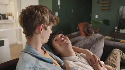 Mixed race young gay couple watching movies together kissing on couch Stock Footage 156378322