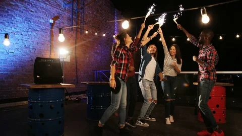Mixed-raced young people having fun and waving with golden sparkler sticks at Stock Footage 81805622