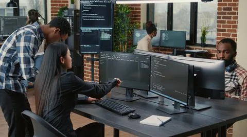 Mixed team of programmers analyzing source code pointing at screens comparing Stock Photos
