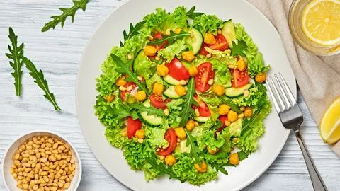 Mixed vivid vegan chickpeas salad, greens, tomato on wood background, minim.. Stock Photos