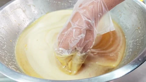 Mixing cake batter or liquid dough with a gloved hand in a bowl. 스톡 동영상 346532407