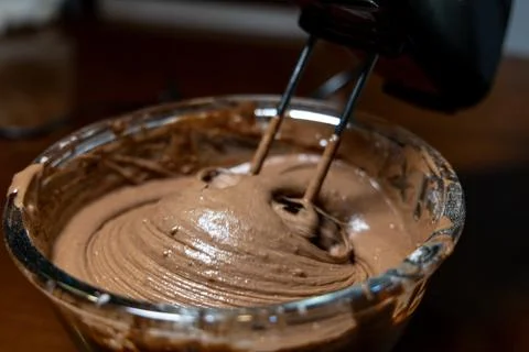 Mixing chocolate cake batter with the help of electric blender in a glass bow Foto stock