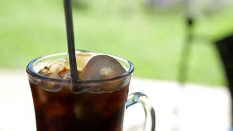 Mixing the cold brew coffee and ice cubes on a sunny day - close up shot Stock Footage 151995424