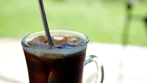 Mixing the cold brew coffee and ice cubes on a sunny day - close up shot Stock Footage 151995429